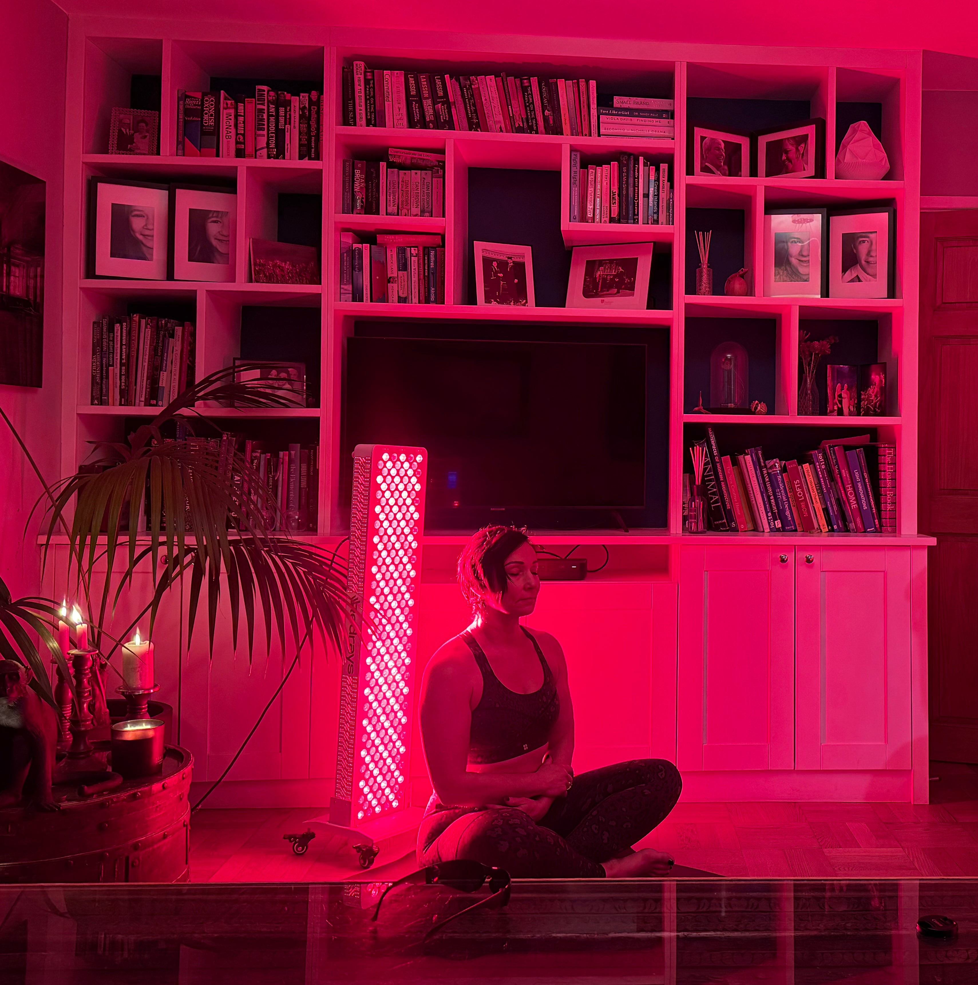 Person sitting in a room using infrared light with a pink hue, surrounded by books and decor.